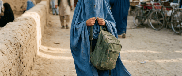 Woman in blue burqa carrying a green backpack through a market street