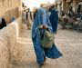 Woman in blue burqa carrying a green backpack through a market street